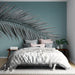 Une chambre moderne avec un papier peint représentant une grande feuille de palmier noire sur un fond bleu apaisant, créant une ambiance tropicale et relaxante.