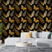 Un salon moderne avec un papier peint noir orné de motifs de papillons dorés et de fougères grises, créant une ambiance élégante et naturelle.