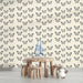 Une chambre d'enfant avec un papier peint crème orné de motifs de papillons noirs, créant une atmosphère douce et ludique.