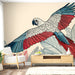 Une pièce lumineuse avec un papier peint illustrant un perroquet coloré aux plumes rouges, bleues et blanches, entouré de feuilles graphiques, créant une ambiance tropicale et vivante.