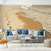 Un salon moderne avec un papier peint représentant une plage dorée, des empreintes de pas sur le sable et des vagues, créant une ambiance sereine et apaisante.