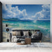Un salon moderne avec un papier peint représentant une mer turquoise sous un ciel bleu parsemé de nuages, évoquant une atmosphère paisible et estivale.