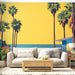 Un salon lumineux avec un papier peint tropical représentant des palmiers colorés sur fond jaune éclatant, évoquant une ambiance estivale et joyeuse.