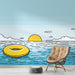 Une chambre lumineuse avec un papier peint illustrant une scène estivale, un soleil jaune brillant et une bouée flottante sur une mer turquoise, dégageant une ambiance joyeuse et relaxante.