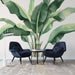 Une salle de séjour moderne avec un papier peint tropical représentant de grandes feuilles de bananier aux teintes vertes, créant une ambiance fraîche et vivante.