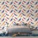 Une chambre douce avec un papier peint aux plumes colorées dans des teintes rose, bleu et jaune sur fond clair, créant une ambiance légère et apaisante.