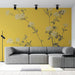 Un salon moderne avec un papier peint jaune vif orné de délicates fleurs blanches et de feuillages, créant une atmosphère chaleureuse et accueillante.