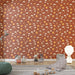 Une chambre d'enfant avec un papier peint ludique représentant des soleils, des nuages et des étoiles sur fond terracotta, créant une ambiance chaleureuse et joyeuse.