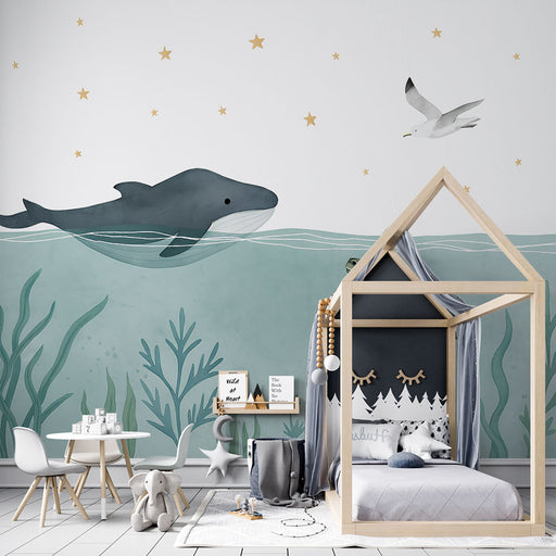Une chambre d’enfant avec un papier peint illustrant un grand cachalot nageant sous l’eau, entouré de plantes marines et d’étoiles dorées, créant une atmosphère douce et imaginative.