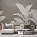 Un salon moderne avec un papier peint représentant de grandes feuilles tropicales blanches sur fond taupe, créant une atmosphère apaisante et élégante.