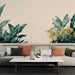 Un salon moderne avec un papier peint tropical représentant de grandes feuilles vertes et dorées sur un fond beige, créant une ambiance chaleureuse et apaisante.
